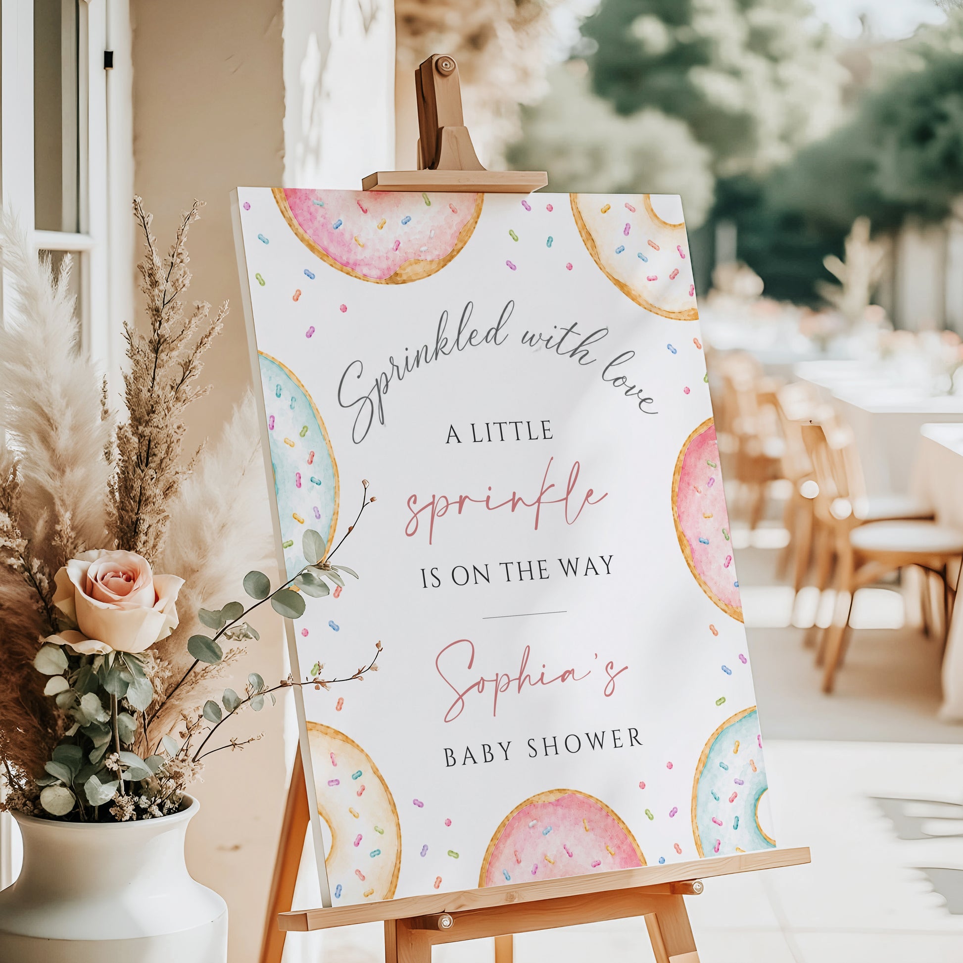 Editable donuts and sprinkles baby shower welcome sign Canva template with watercolour pastel donuts, rainbow sprinkles, and script typography on a soft white background