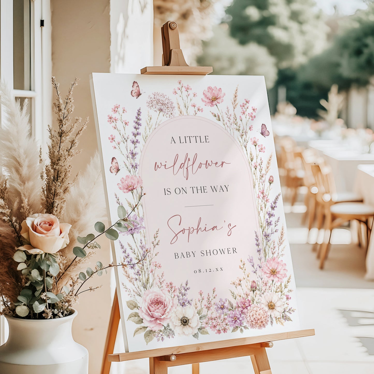 Editable wildflower baby shower welcome sign Canva template with watercolour roses, lavender, cosmos, blush arch, and butterfly details in soft pink and purple tones