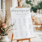 Modern black and white wedding seating chart sign template with oversized calligraphy script and 12 table layout, editable in Canva