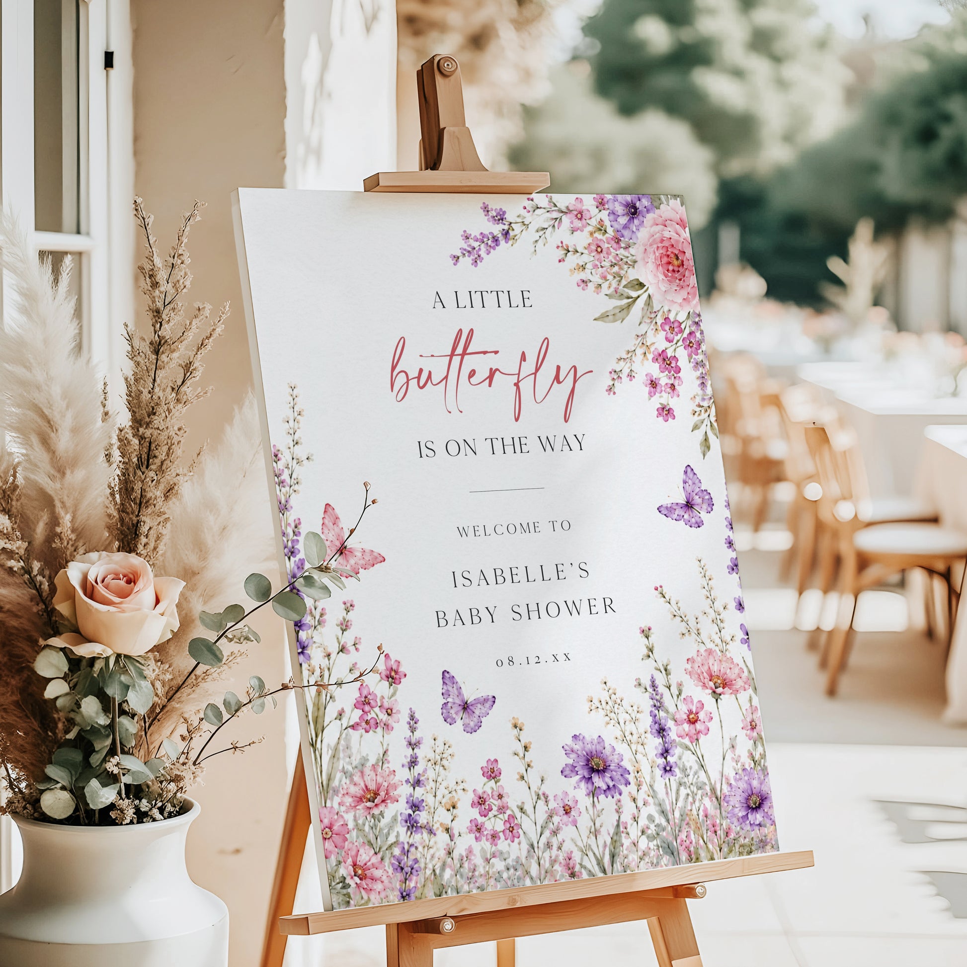Editable butterfly baby shower welcome sign Canva template with watercolour pink and purple butterflies, peonies, lavender, and wildflower meadow on a white background, shown as a hanging print mockup