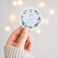 Editable blueberry baby shower round thank you sticker Canva template with watercolour blueberry wreath, white blossoms, blue ribbon bows, and script typography on a soft blue background
