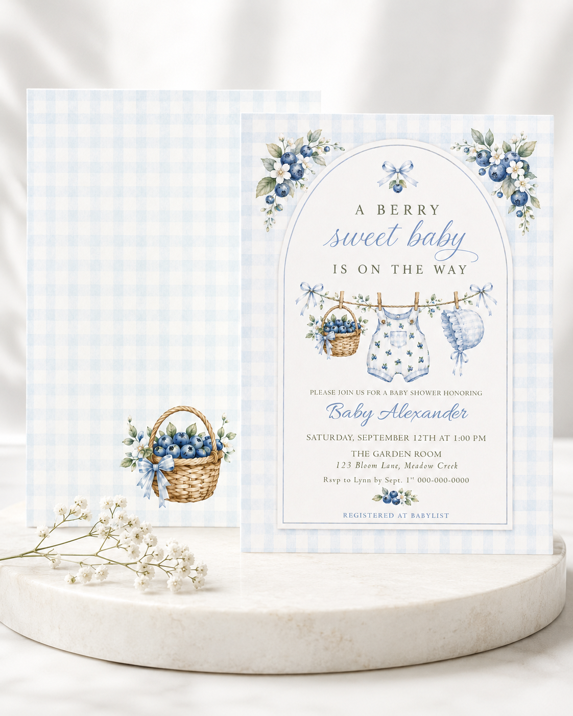 Editable blue gingham boy baby shower invitation Canva template with watercolour blueberries, clothesline scene with romper and bonnet, and script typography, shown with front and back of card