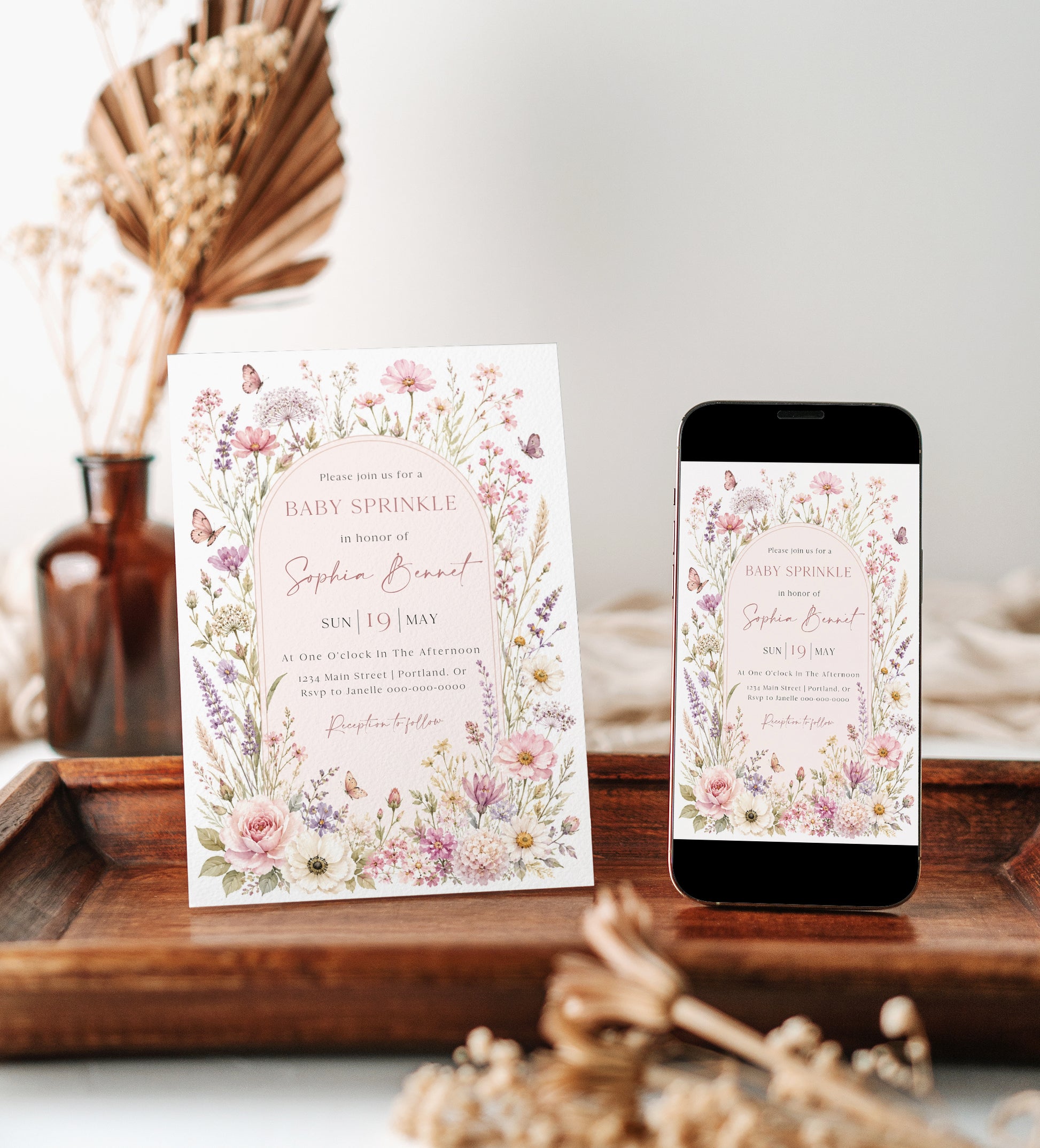 Editable wildflower baby sprinkle invitation Canva template with watercolour botanicals, blush arch, butterfly details, and script typography on a soft pink background