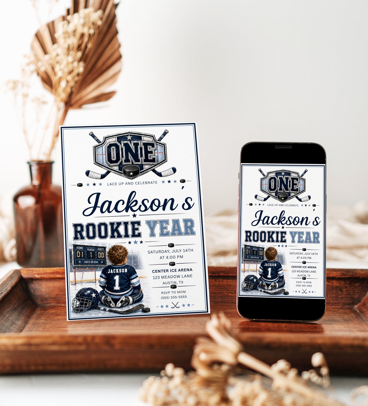 Rookie Year first birthday invitation with little hockey player, ice rink, scoreboard, helmet, hockey sticks, puck, and navy blue birthday party details