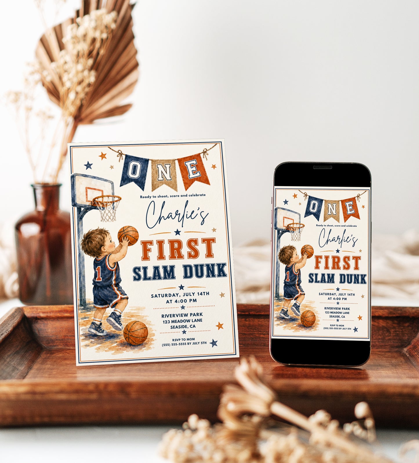 Basketball first birthday invitation featuring a little boy shooting a basketball, hoop, ONE banner, stars and navy and orange sports details.
