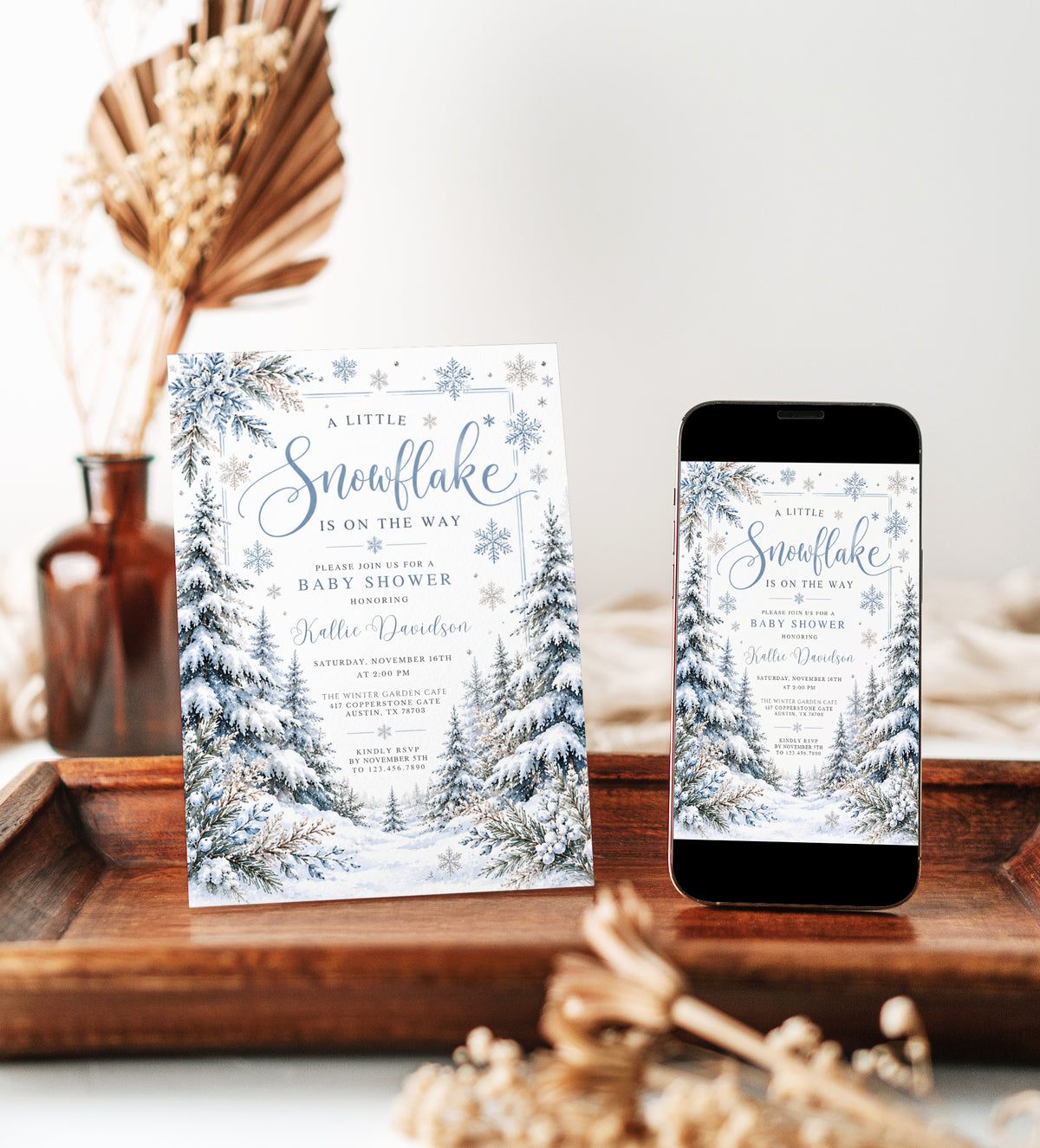 Winter baby shower invitation with blue snowflakes, snow-covered evergreen trees, frosted foliage, and A Little Snowflake Is on the Way wording on white