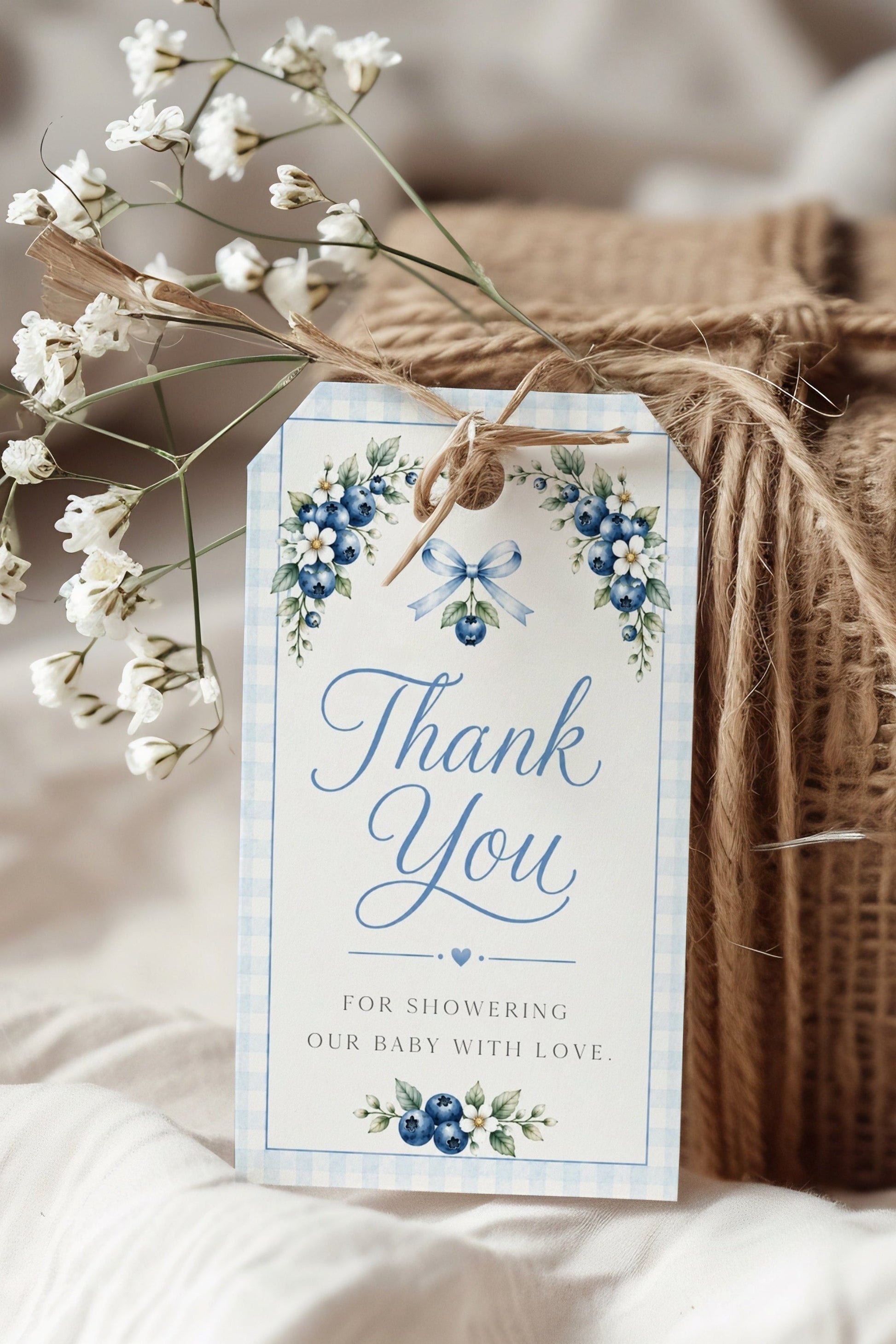 Editable blueberry baby shower favor hang tag Canva template with watercolour blueberry clusters, white blossoms, blue ribbon bow, and script typography on a cream background with blue gingham border