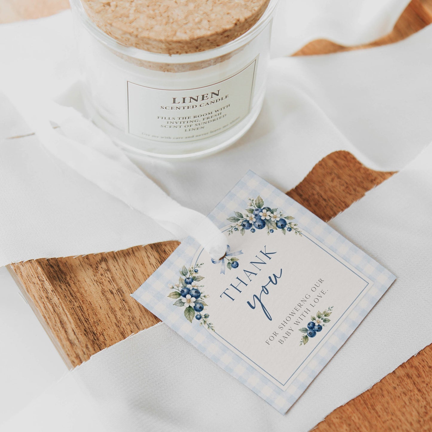 Editable blueberry baby shower gift tag Canva template with watercolour blueberry clusters, white blossoms, blue ribbon bow, and script typography on a cream arch with blue gingham background