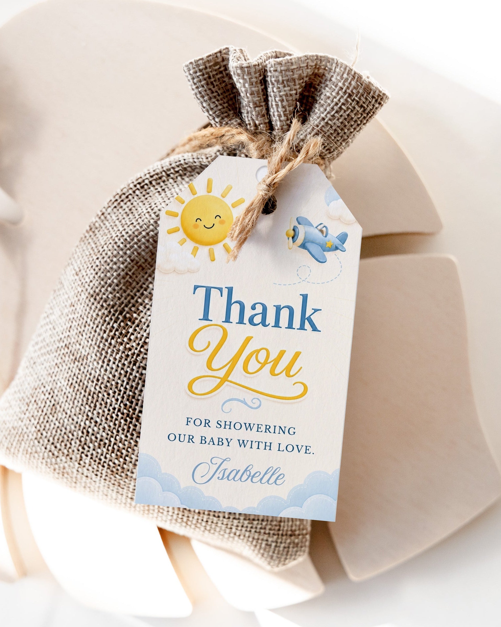 Editable here comes the son baby shower favor hang tag Canva template with smiling sun, blue toy airplane, fluffy clouds, and bold navy and golden script typography on a warm cream background