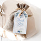 Editable blueberry baby shower favor hang tag Canva template with watercolour blueberry clusters, white blossoms, blue ribbon bow, and script typography on a cream background with blue gingham border