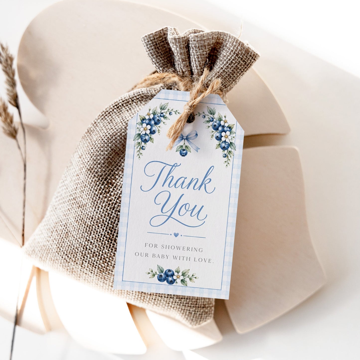 Editable blueberry baby shower favor hang tag Canva template with watercolour blueberry clusters, white blossoms, blue ribbon bow, and script typography on a cream background with blue gingham border