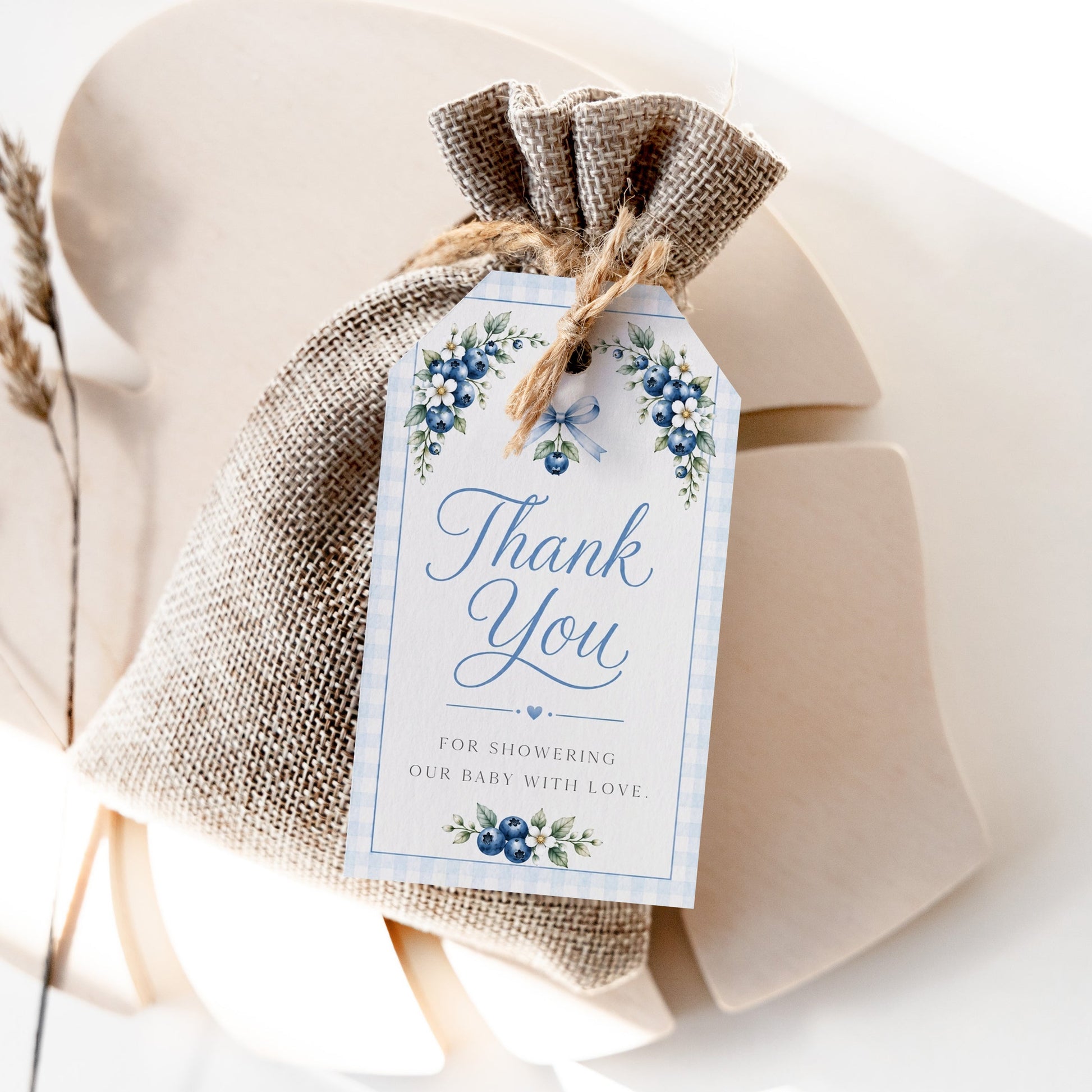 Editable blueberry baby shower favor hang tag Canva template with watercolour blueberry clusters, white blossoms, blue ribbon bow, and script typography on a cream background with blue gingham border