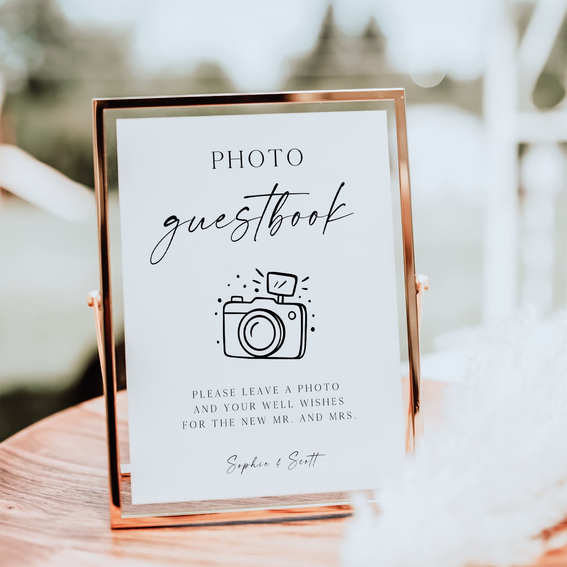 Minimalist black and white wedding photo guestbook sign template with calligraphy script and hand-drawn camera illustration, editable in Canva