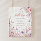 Editable butterfly baby shower welcome sign Canva template with watercolour pink and purple butterflies, peonies, lavender, and wildflower meadow on a white background, shown as a hanging print mockup