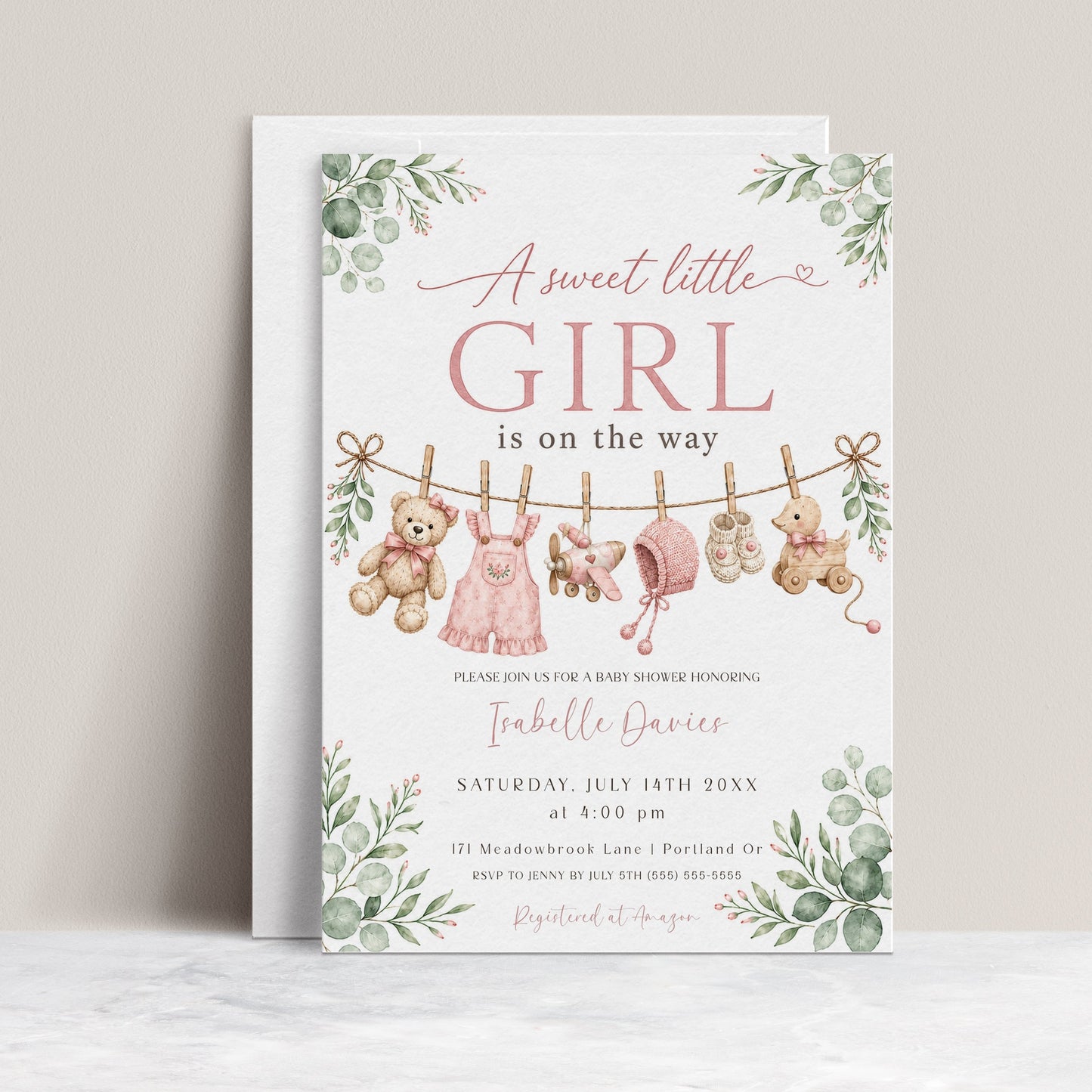 Sweet little girl baby shower invitation with hanging baby clothes, a teddy bear, and greenery in soft pink and sage
