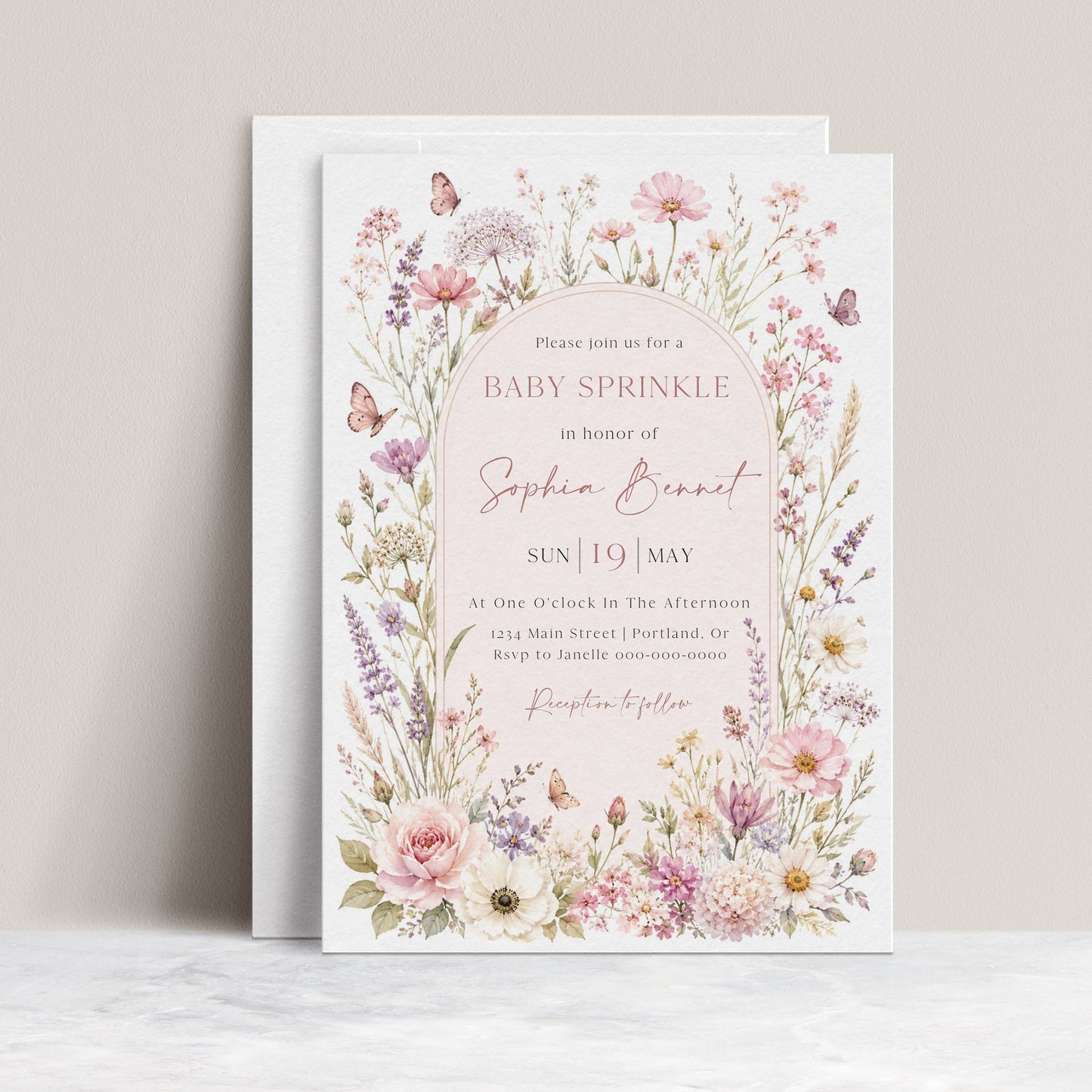 Editable wildflower baby sprinkle invitation Canva template with watercolour botanicals, blush arch, butterfly details, and script typography on a soft pink background