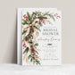 Winter bridal shower invitation with a flowing ivory bow, evergreen branches, red and white berries, snow-dusted pinecones, and gold accents on a white background