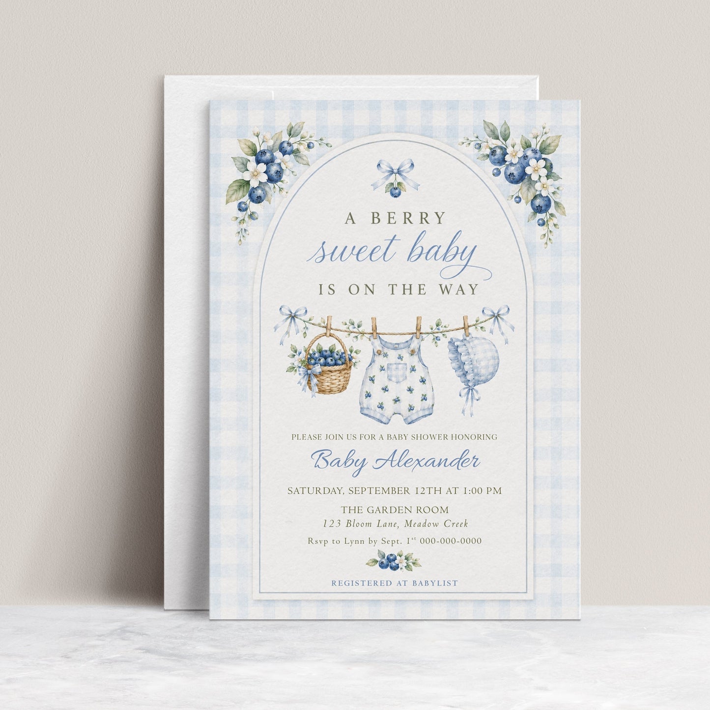 Editable blue gingham boy baby shower invitation Canva template with watercolour blueberries, clothesline scene with romper and bonnet, and script typography, shown with front and back of card