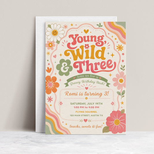 Young wild and three birthday invitation with groovy retro lettering, colorful flowers, rainbow waves, hearts, stars, and boho pink orange sage details