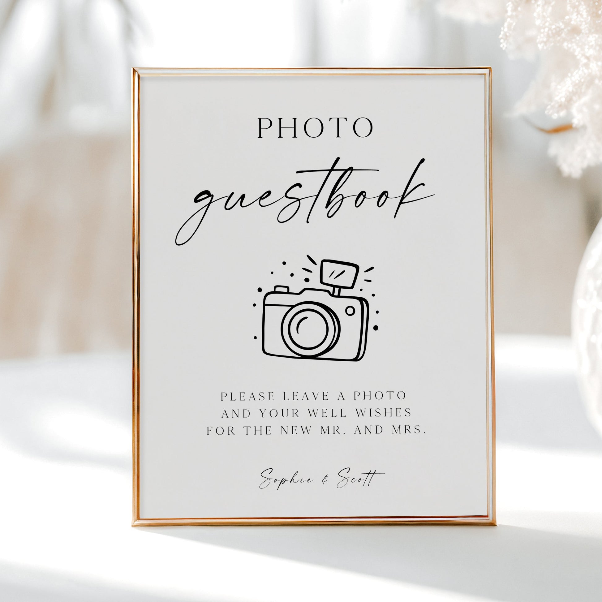 Minimalist black and white wedding photo guestbook sign template with calligraphy script and hand-drawn camera illustration, editable in Canva