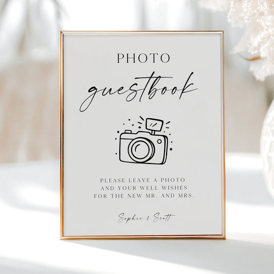 Minimalist black and white wedding photo guestbook sign template with calligraphy script and hand-drawn camera illustration, editable in Canva