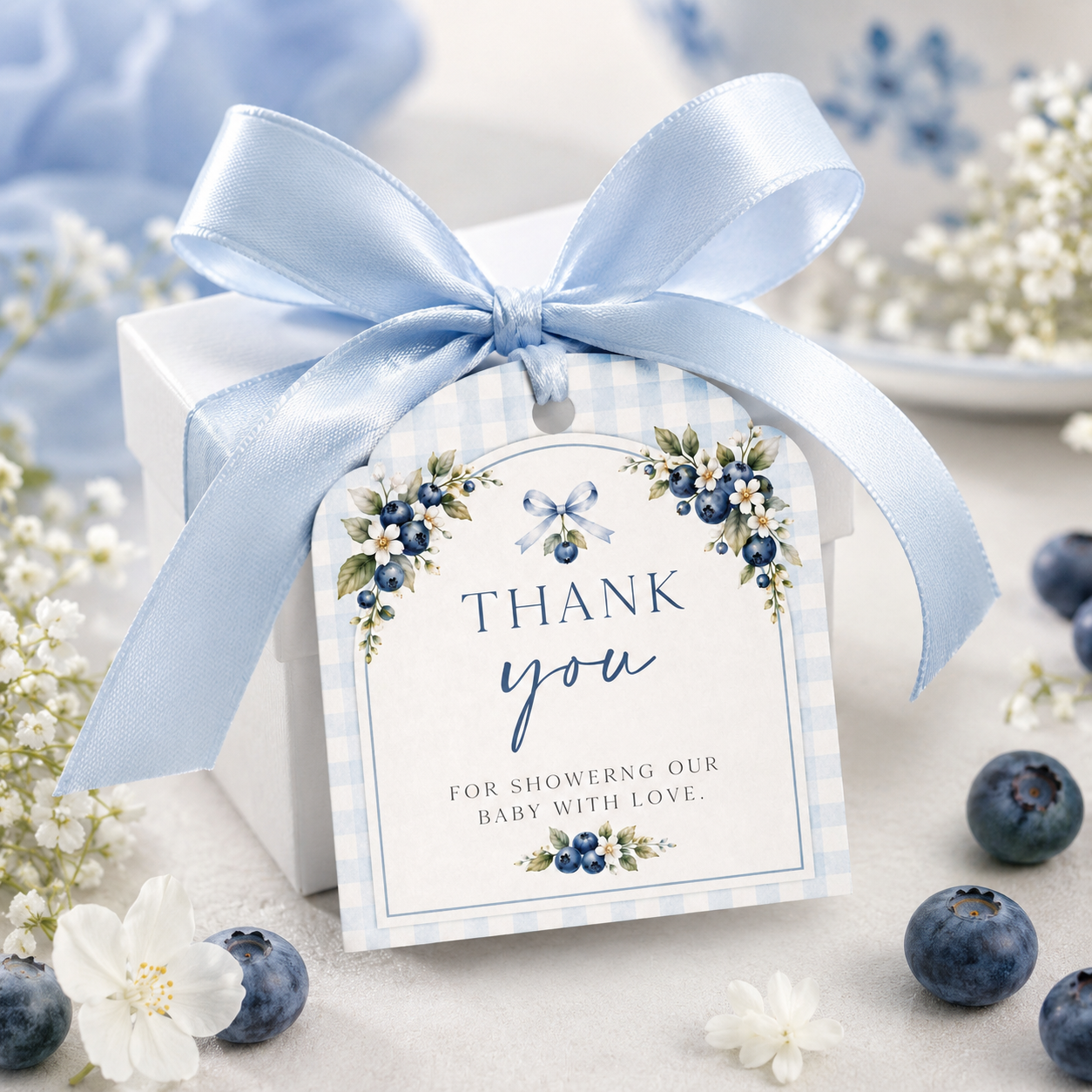 Editable blueberry baby shower gift tag Canva template with watercolour blueberry clusters, white blossoms, blue ribbon bow, and script typography on a cream arch with blue gingham background